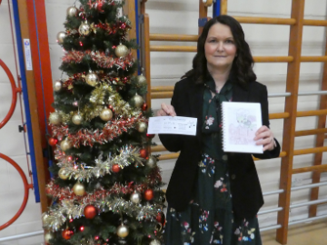 Lady holding papers, stood by Christmas Tree in sports hall