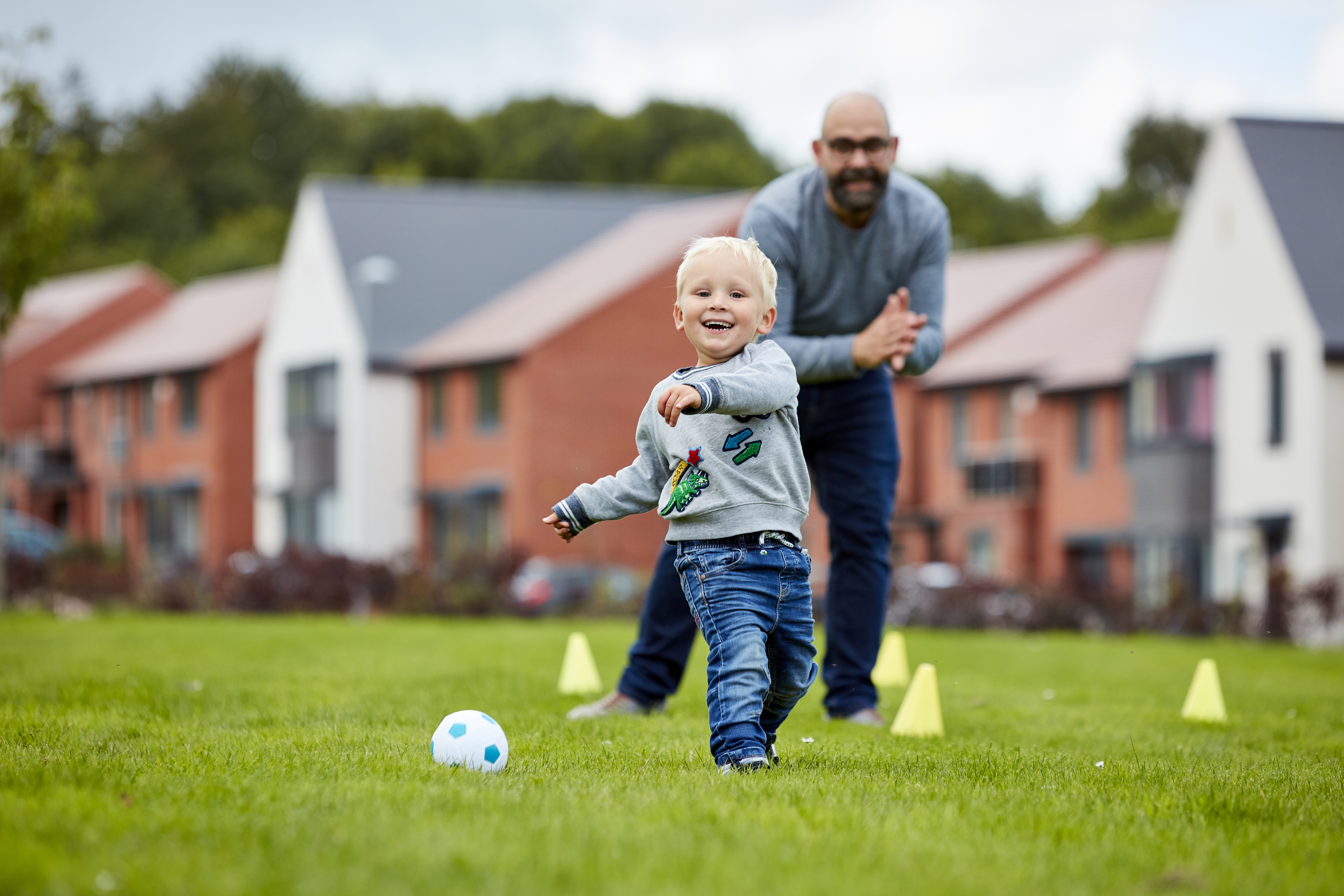 Dad and son playing football in front of new Taylor Wimpey homes