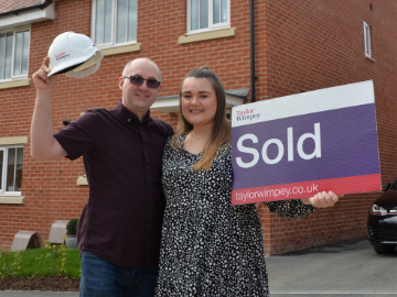 Young couple stood next to sold sign