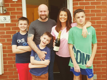 Family of 5 holding bottle of fizz outside new home