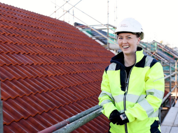 Girl in high vis jacket and hard hat on a rooftop scaffold