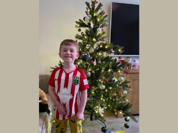 Young boy in striped t-shirt, next to Christmas tree