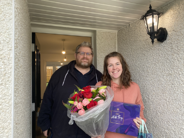 Couple outside home with bouquet of flowers and chocolates