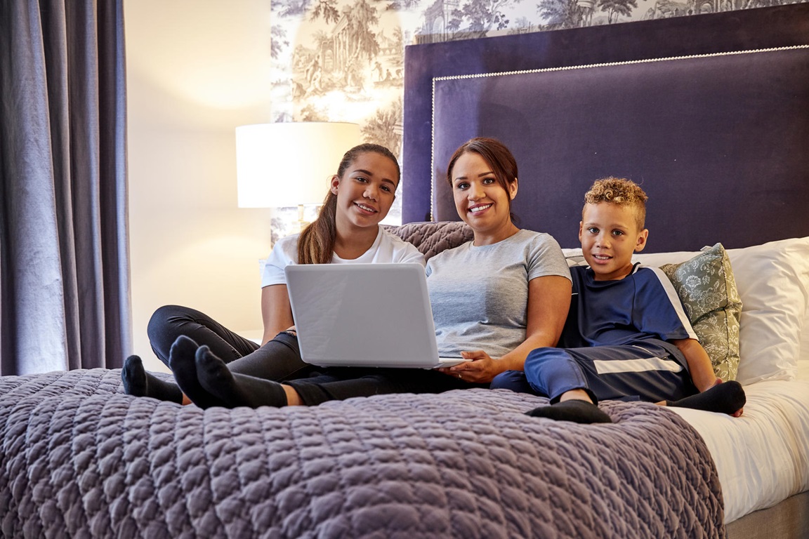 Mother and children with laptop smiling on bed